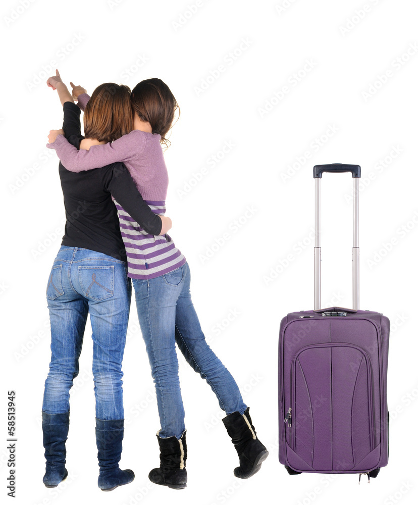Two women traveling with suitcas and pointing at wall. Two women traveling with suitcas and pointing at wall.