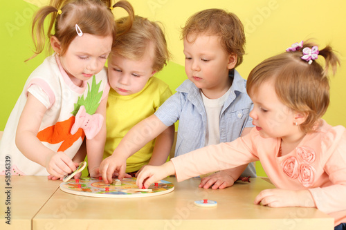Two boys and two girls doing together wooden puzzle