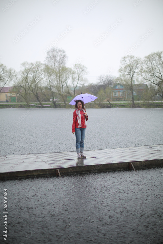 A young woman with umbrella stands on wooden pier
