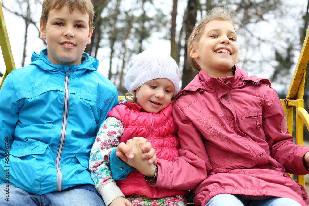 Cheerful boy and two girls in bright jackets on swings Cheerful boy and two girls in bright jackets on swings