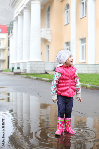 Happy girl in bright clothes standing in a puddle