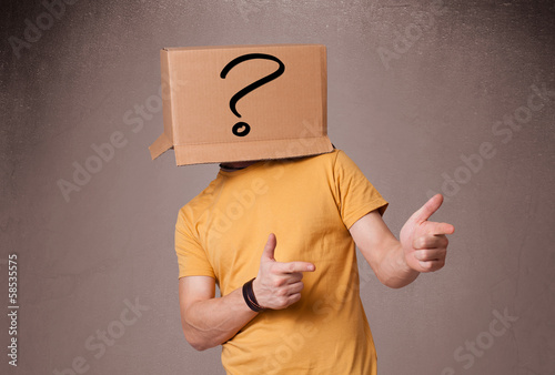 Young man gesturing with a cardboard box on his head with questi photo