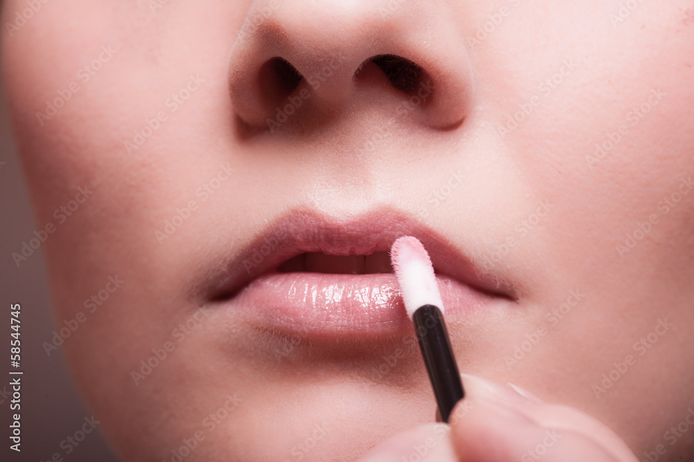 Naklejka premium Makeup. Girl applying lipgloss lipstick on lips. Part of face.