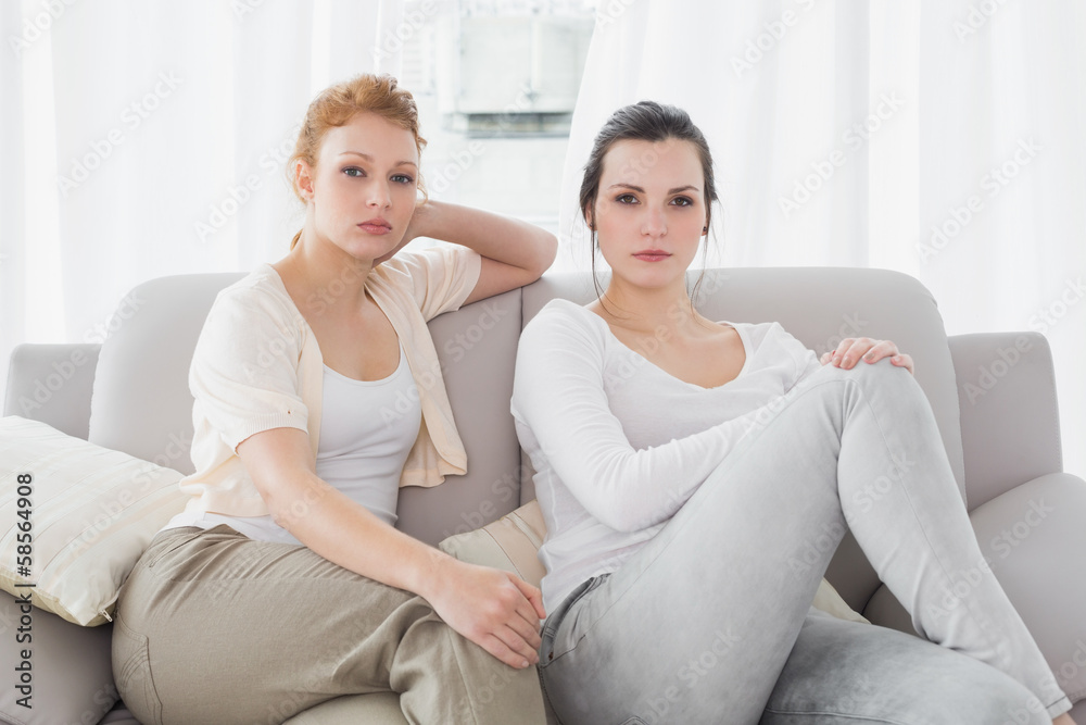 Two serious female friends sitting on sofa in the living room