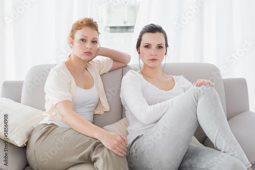 Two serious female friends sitting on sofa in the living room