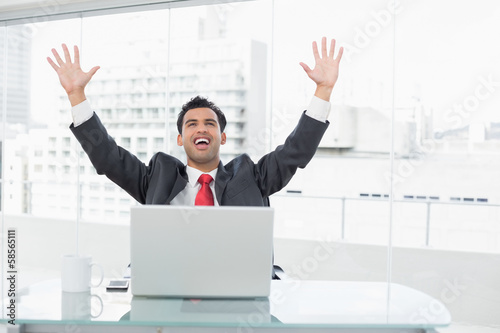 Businessman cheering in front of laptop at office desk