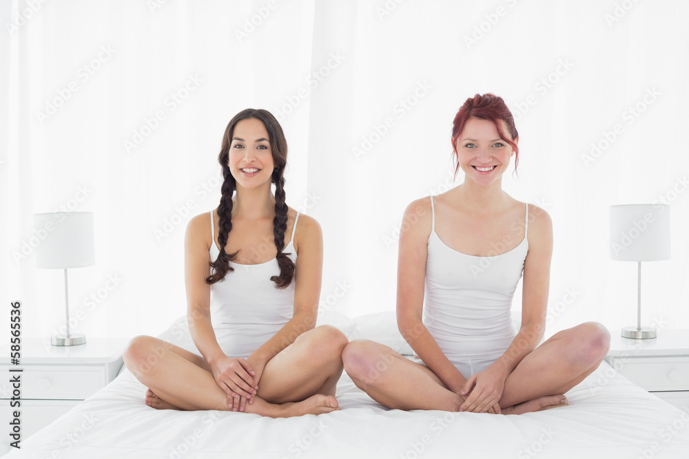 Happy female friends in white tank tops sitting on bed Happy female friends in white tank tops sitting on bed