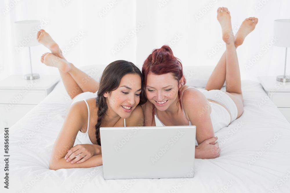 Relaxed female friends using laptop in bed Relaxed female friends using laptop in bed
