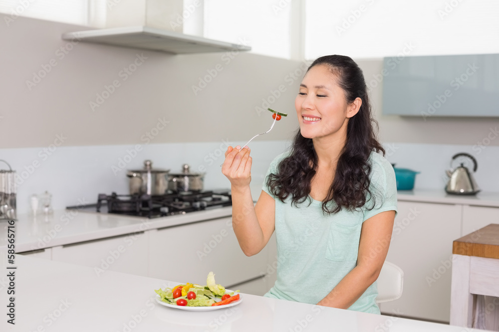 Happy young woman eating salad in kitchen