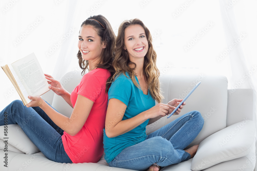 Smiling friends with book and digital tablet sitting at home Smiling friends with book and digital tablet sitting at home