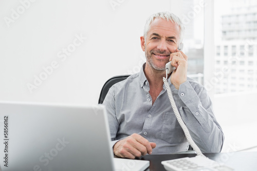 Smiling businessman on call in front of laptop at office desk photo
