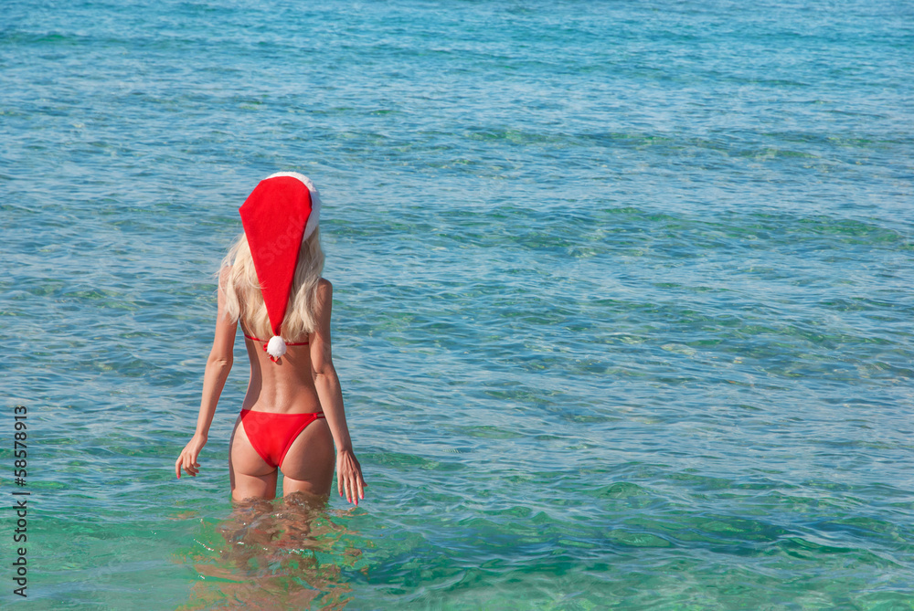 Beautiful blonde woman in red christmas hat on sea beach. New ye