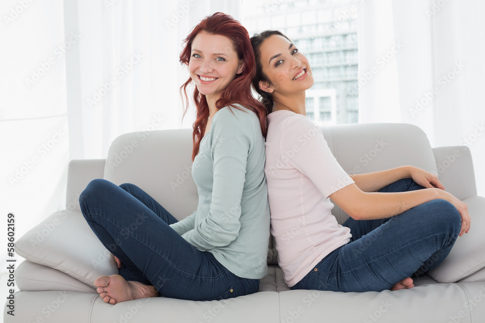 Smiling female friends sitting back to back at home Smiling female friends sitting back to back at home