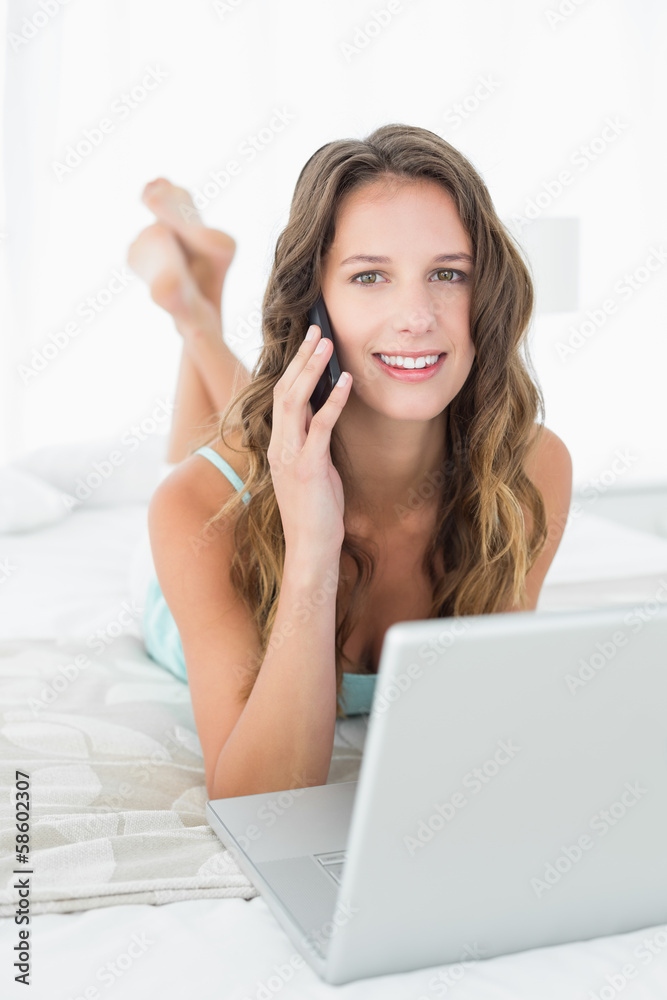 Relaxed woman using mobile phone and laptop in bed Relaxed woman using mobile phone and laptop in bed