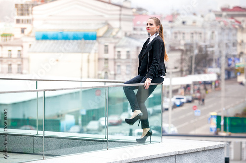 Beautiful businesswoman sitting on railings against city view