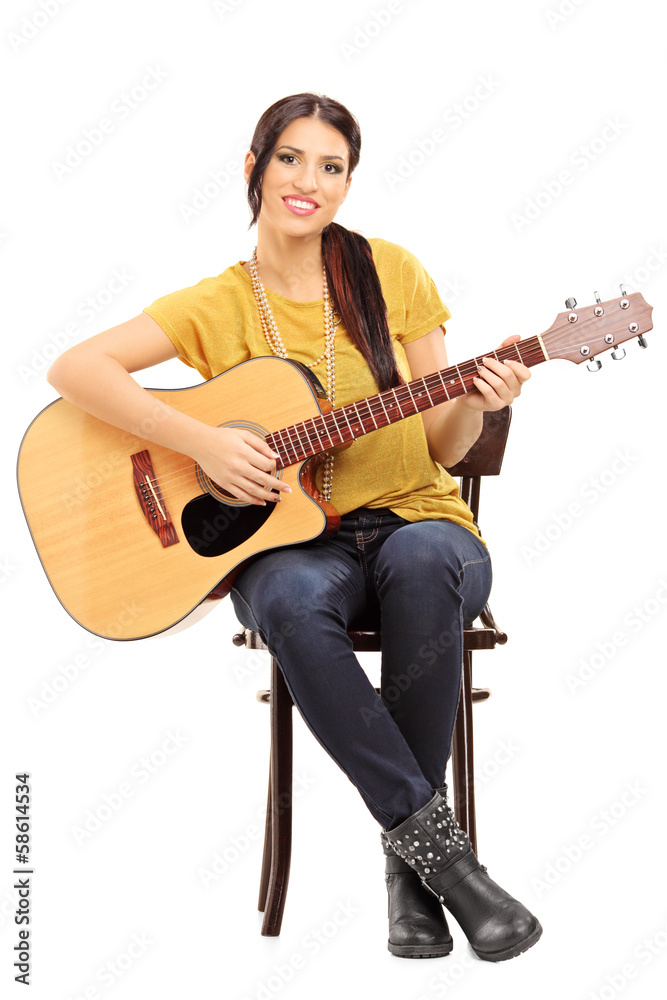 Young female musician on a chair holding an acoustic guitar Young female musician on a chair holding an acoustic guitar