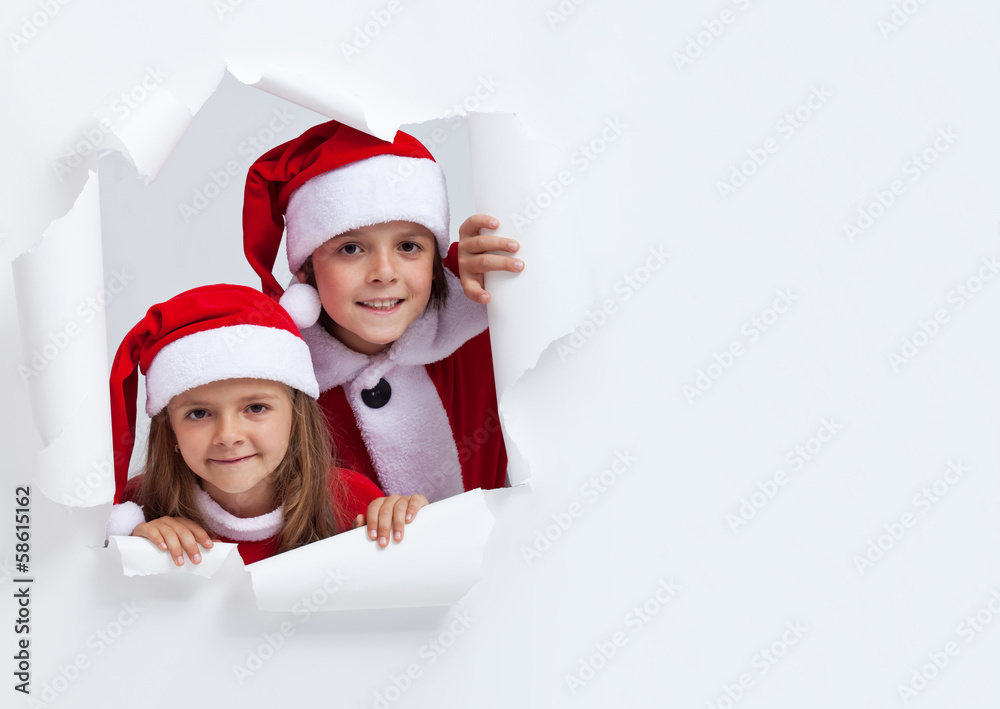 Happy kids in santa outfits looking through hole in paper Happy kids in santa outfits looking through hole in paper