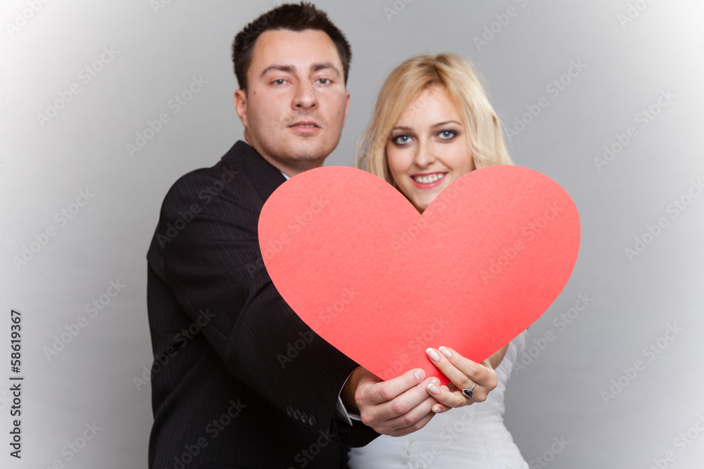 Portrait of happy bride and groom with red heart on gray