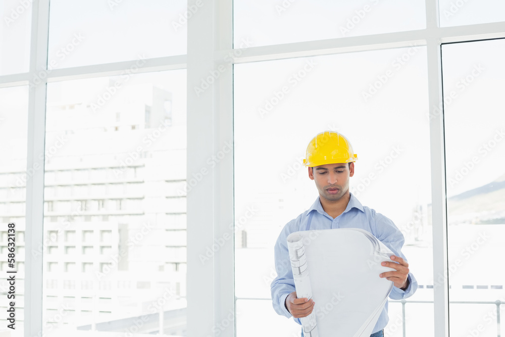 Architect in yellow hard hat looking at blueprint in office Architect in yellow hard hat looking at blueprint in office