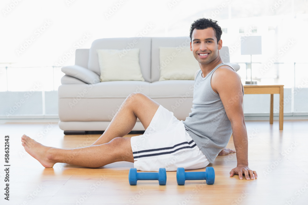 Relaxed man sitting on floor with dumbbells in the living room