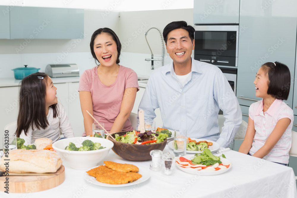 Cheerful family of four enjoying healthy meal in kitchen