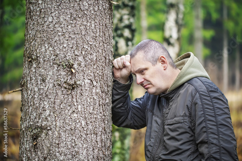 Depressed man leaning on a tree