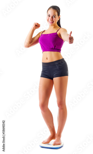 Young sporty girl on scales shows ok gesture