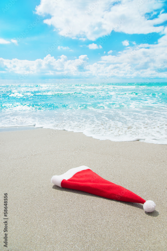 Santa Claus hat on seashore against waves and blue sky