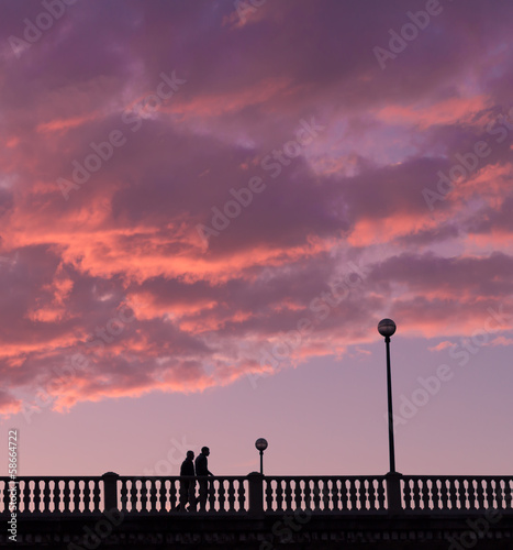 Two close people walking on a bridge, in the evening