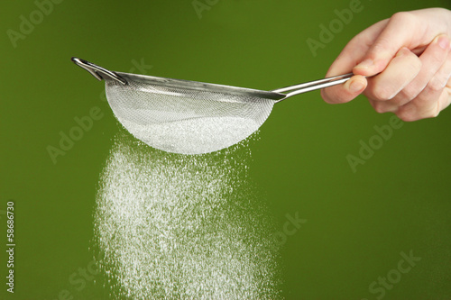 Sieve and powdered sugar on green background photo