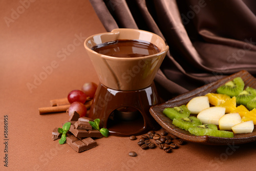 Chocolate fondue with fruits  on  brown background