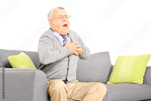 Valokuva Senior man seated on a sofa having a heart attack