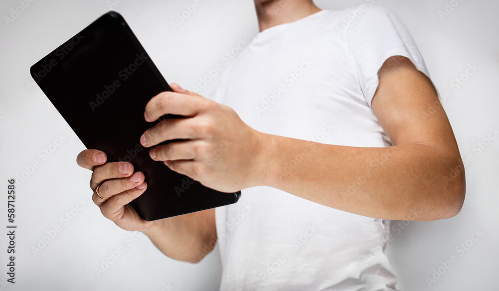 Man in white t-shirt using tablet pc, white wall on background Man in white t-shirt using tablet pc, white wall on background