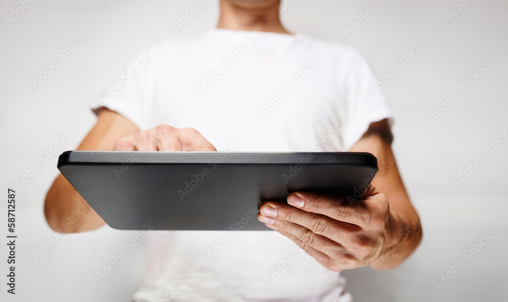 Man in white t-shirt using tablet pc, white wall on background Man in white t-shirt using tablet pc, white wall on background