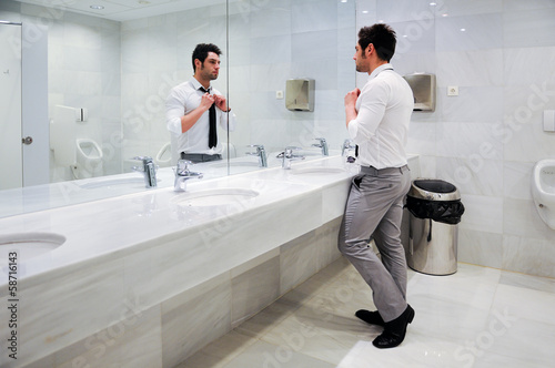 Quadro su tela Man getting dressed in a public restroom with mirror