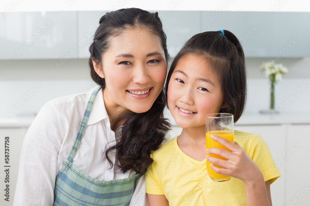Girl holding orange juice with her mother in kitchen Girl holding orange juice with her mother in kitchen