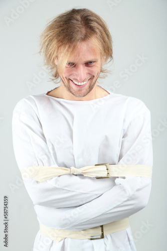 Mentally ill man in strait-jacket on gray background