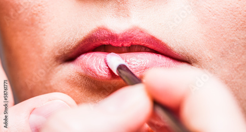 Makeup. Girl applying lipgloss lipstick on lips. Part of face.