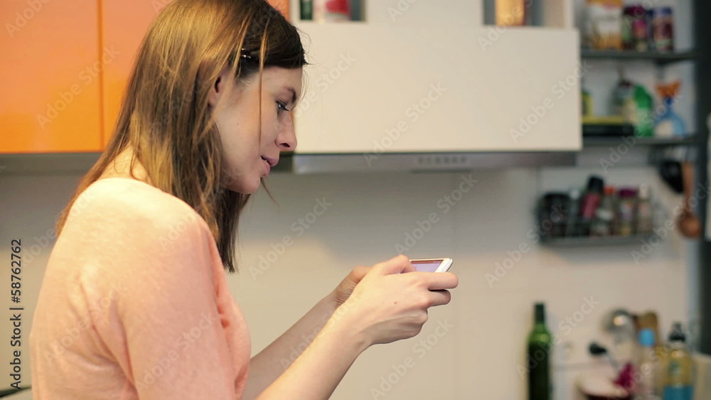 Woman texting on smartphone and drinking coffee in kitchen Woman texting on smartphone and drinking coffee in kitchen