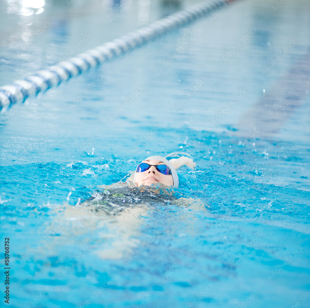 Young girl in goggles swimming back crawl stroke style