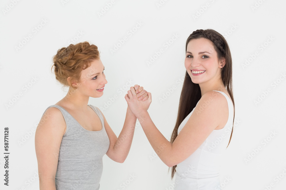 Portrait of two casual young female friends arm wrestling Portrait of two casual young female friends arm wrestling