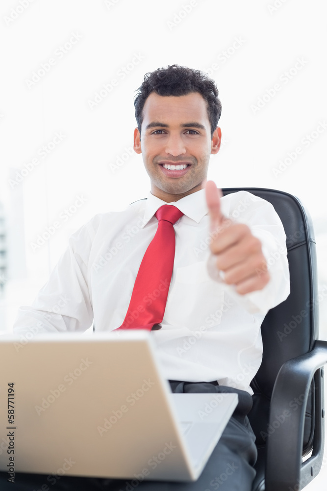 Smiling businessman with laptop gesturing thumbs up