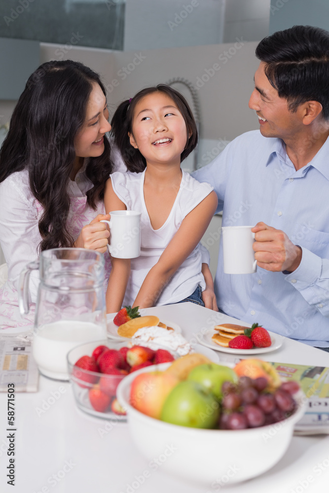 Happy young girl enjoying breakfast with parents Happy young girl enjoying breakfast with parents