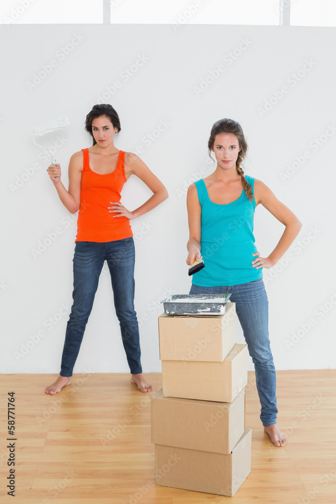 Female friends with paint brushes in a new house Female friends with paint brushes in a new house