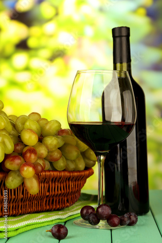 Ripe grapes in wicker basket, bottle and glass of wine,