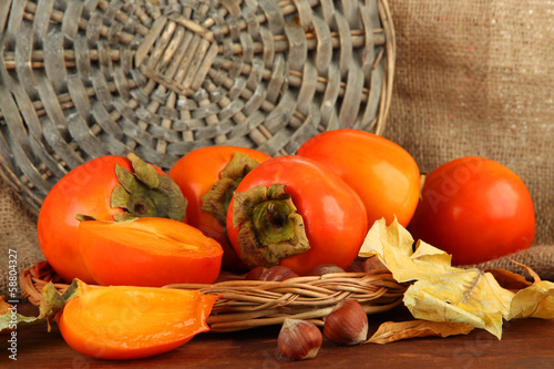 Ripe persimmons with nuts on table on wicker background