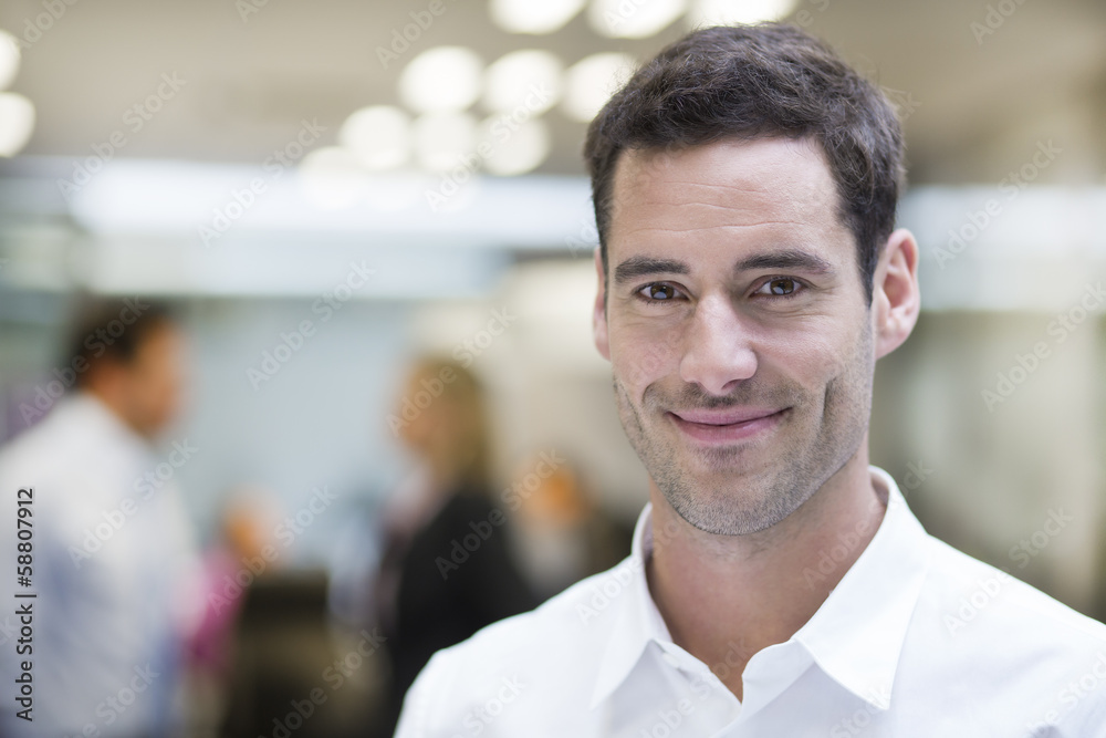 Smiling Businessman posing while colleagues talking together Smiling Businessman posing while colleagues talking together