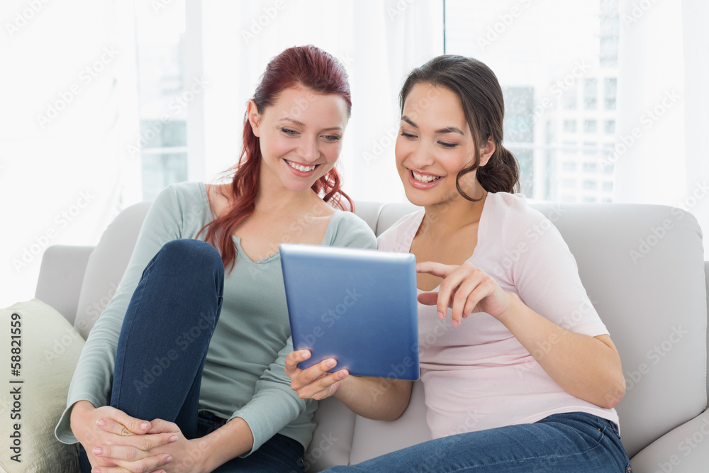 Happy relaxed female friends using digital tablet at home Happy relaxed female friends using digital tablet at home