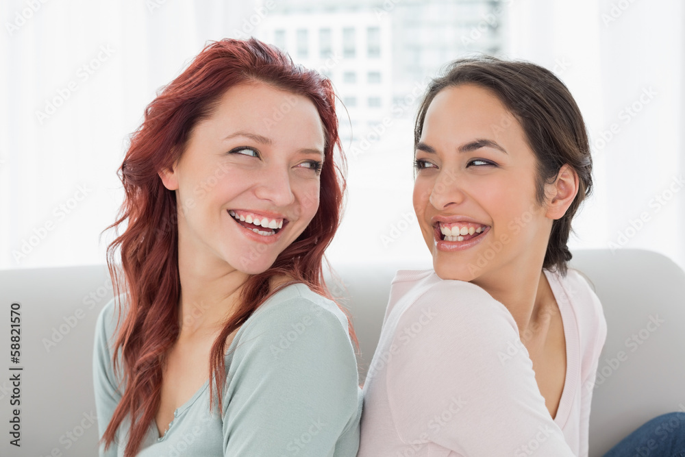 Beautiful young female friends sitting back to back at home Beautiful young female friends sitting back to back at home