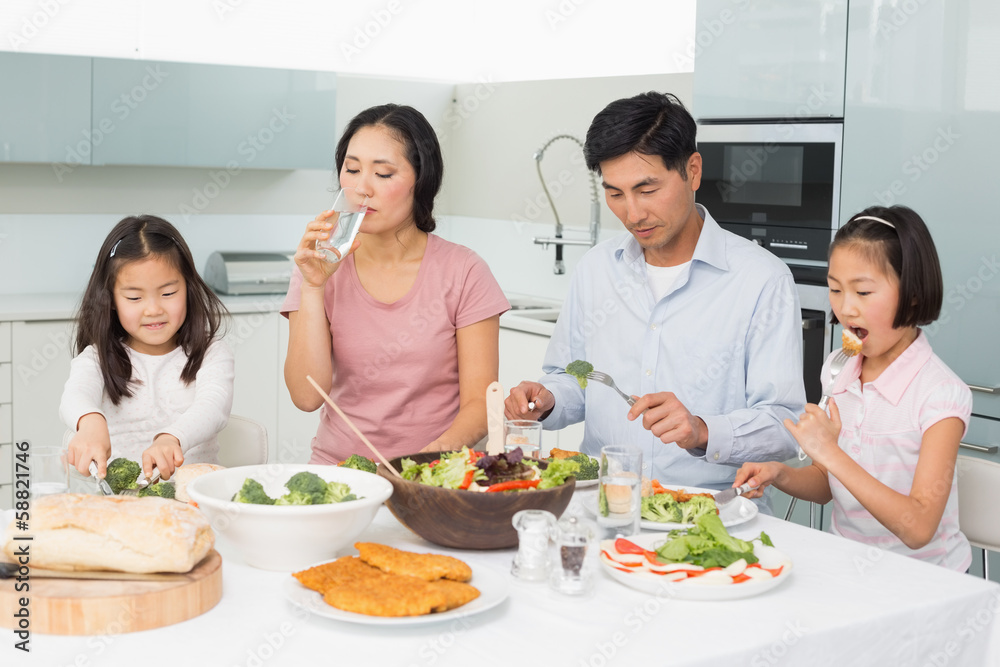 Young family of four enjoying healthy meal in kitchen Young family of four enjoying healthy meal in kitchen